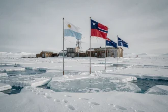 Station de recherche en Antarctique avec plusieurs drapeaux nationaux plantés dans la neige, illustrant les revendications territoriales sur le continent antarctique